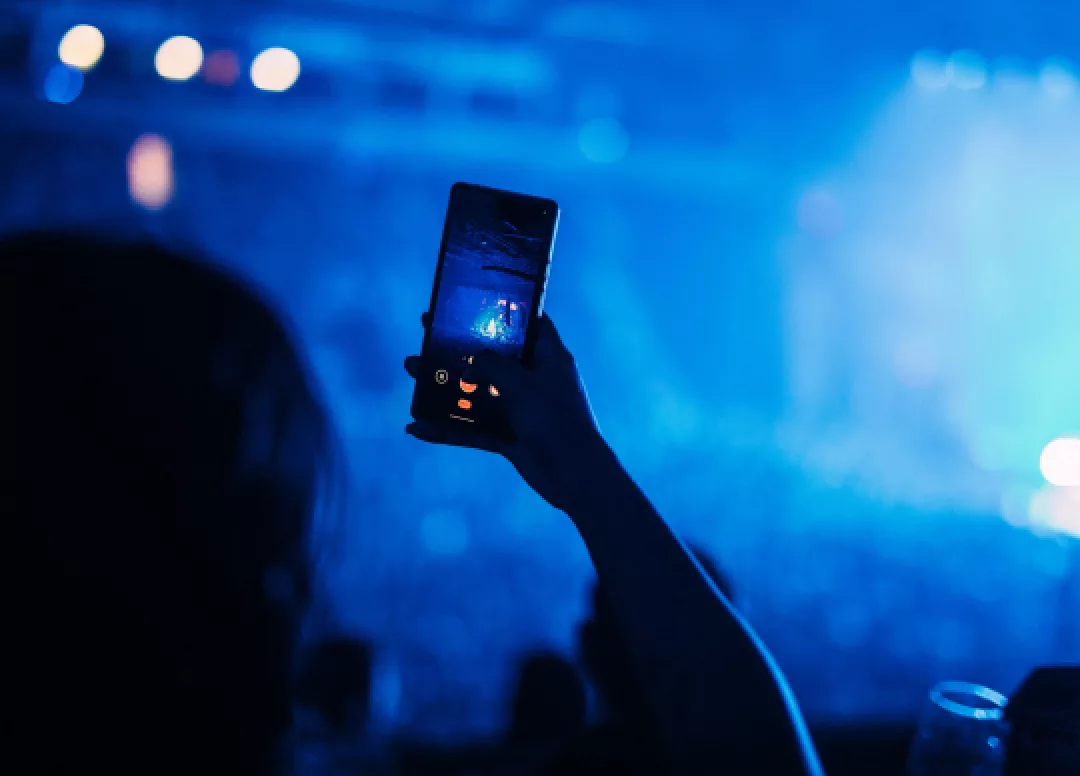 A concertgoer holding up a smartphone to record a live performance on stage at the arena.
